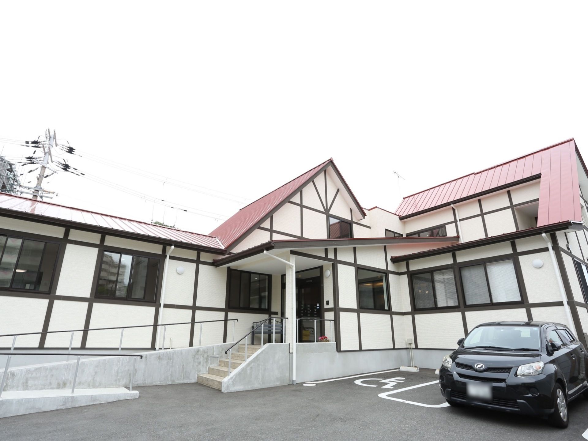 赤い屋根が印象的な２階建ての施設。車椅子優先の駐車スペースが確保されており、玄関前にはスロープも設置されている。