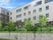 グレー系の4階建ての建物が高台に建っていて、周りには草木も植えられている。男女が道を歩いている。
