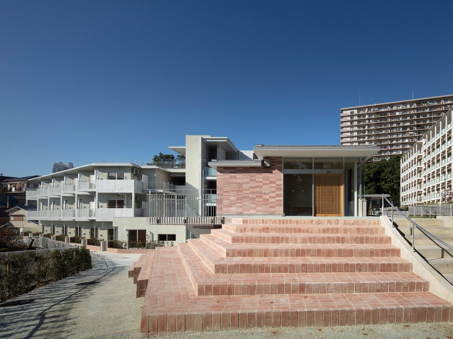奥には白い住宅の建物があり、手前にはレンガでできた階段があり、階段を上ったところにはレンガの外壁の建物が建っている。