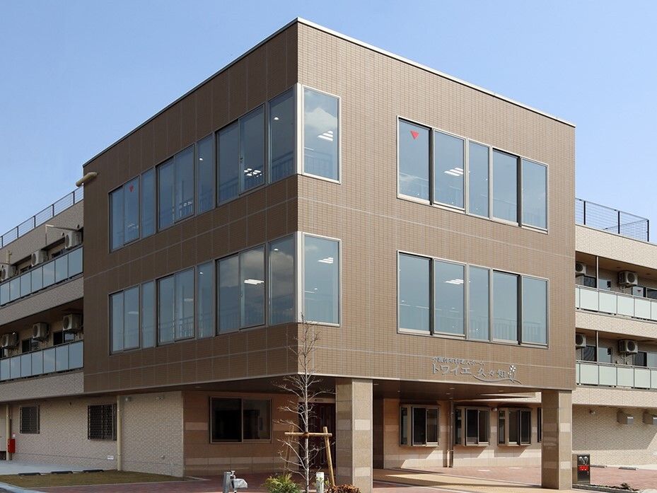 ３階建ての建物はブラウン系で、各フロアにベランダがあり、建物の前に木が1本植えられている。