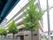 各フロアにベランダがある4階建ての建物の周りには草木が植えられ、建物の周辺にはマンションのようなビルがある。