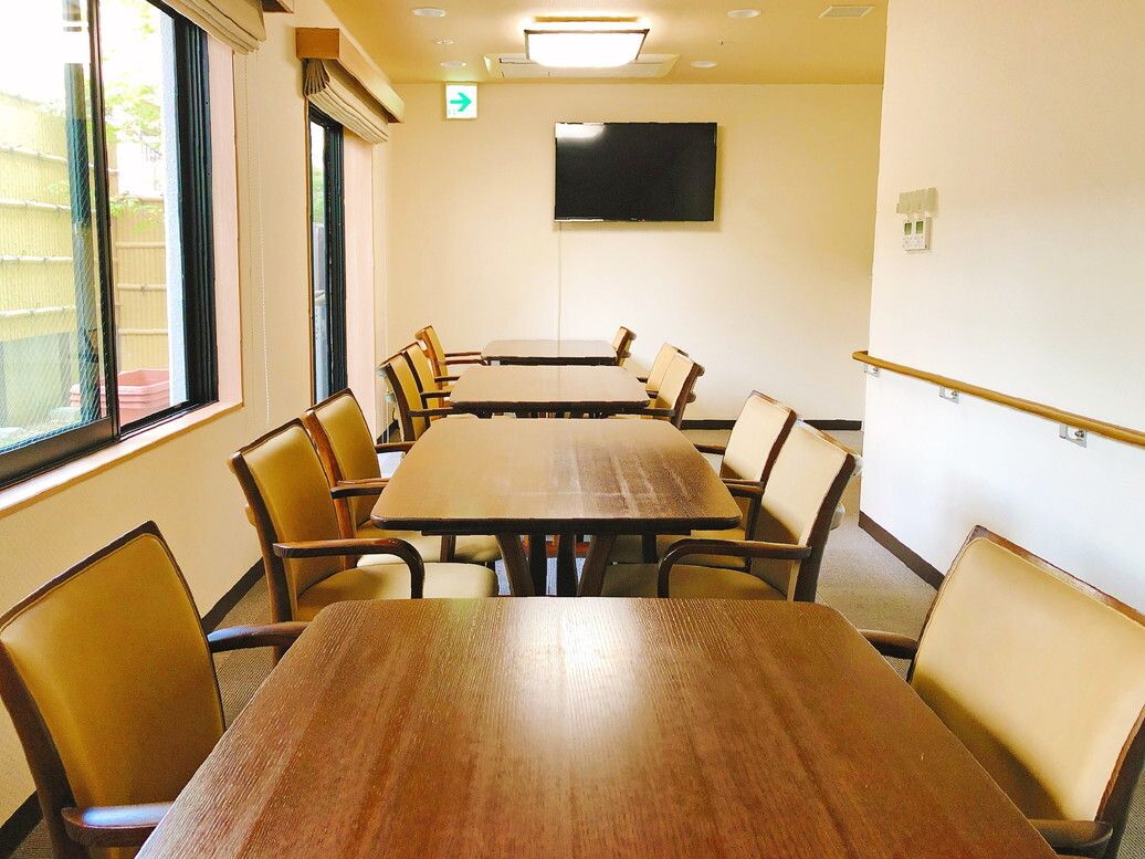 大きな壁掛けテレビが設置された食堂には木製のダイニングテーブルが複数置かれている。
