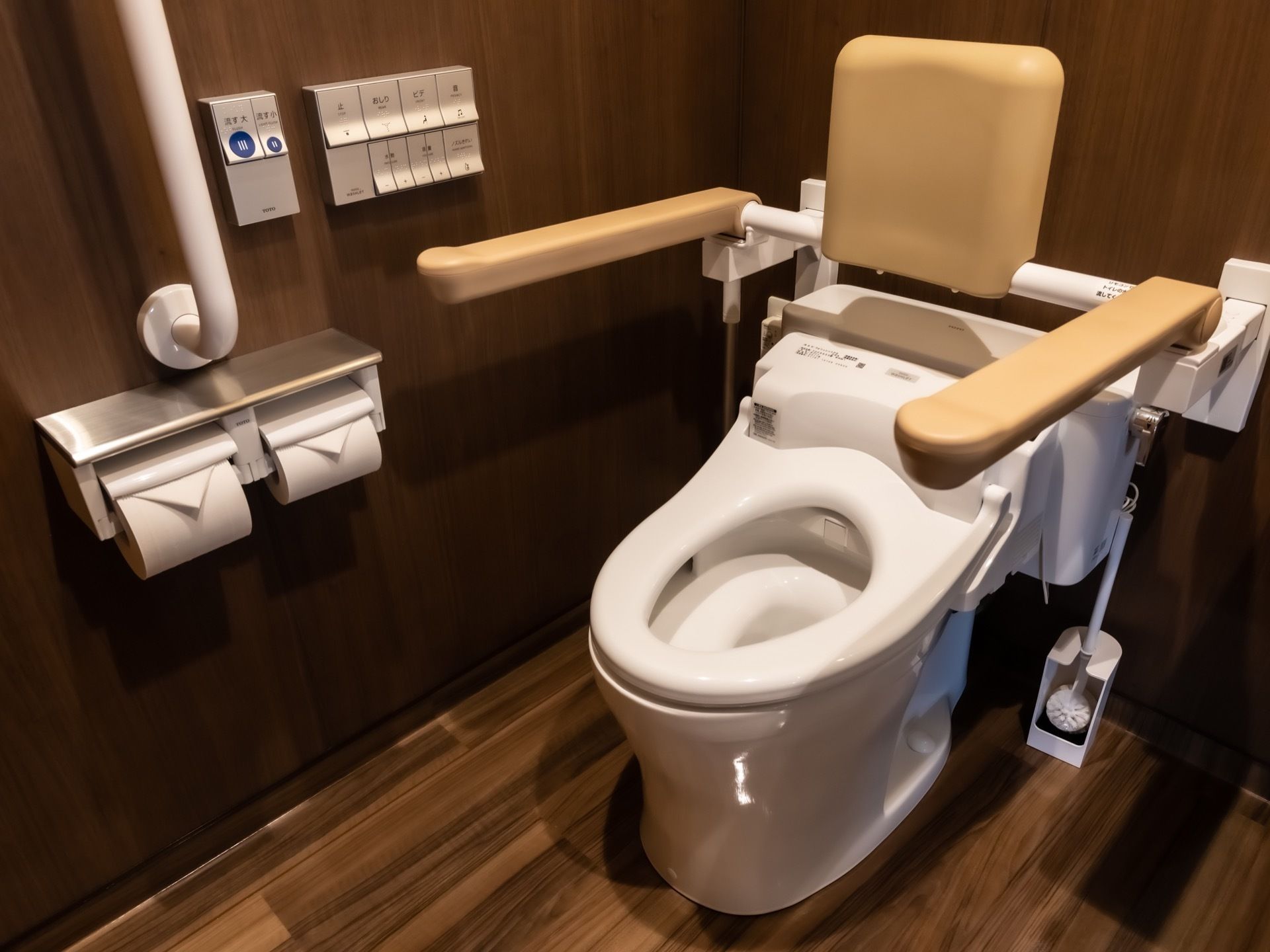 トイレの内部はシックなブラウンで統一され、オシャレで高級感がある。安全のため、便器には背もたれ付きの手すりがついている。