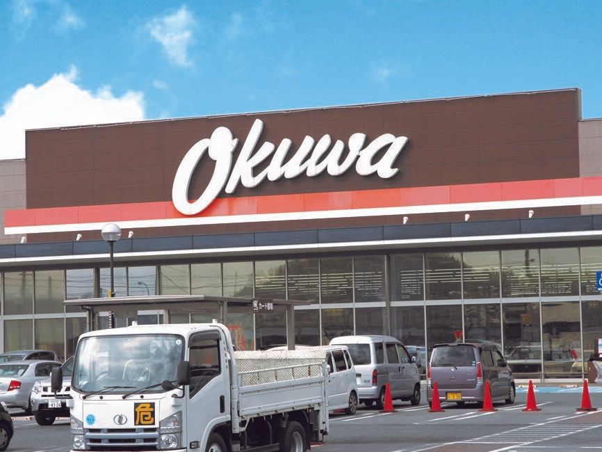 「Okuwa」と書かれた看板が目印のブラウン系の大きな店舗。敷地内には広い駐車場もあり、車がたくさん止まっている。