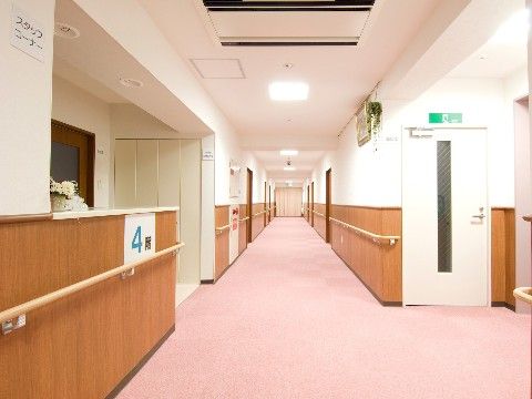 廊下は広く、淡いピンクの床に木の色合いが温かい雰囲気。転倒防止のため手すりを配置し、障害物もなく、車椅子で安心してご移動いただける。