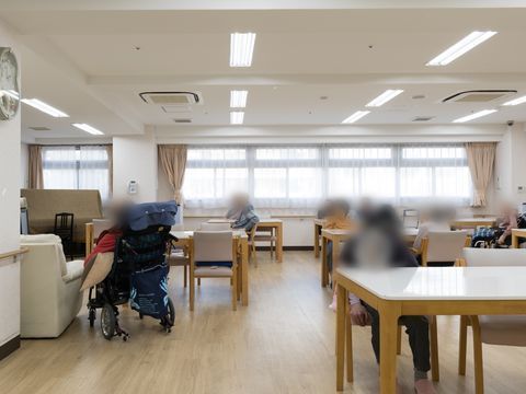 白いテーブルのセットが配置され数名の入居者様が椅子に腰掛けられている共有スペース