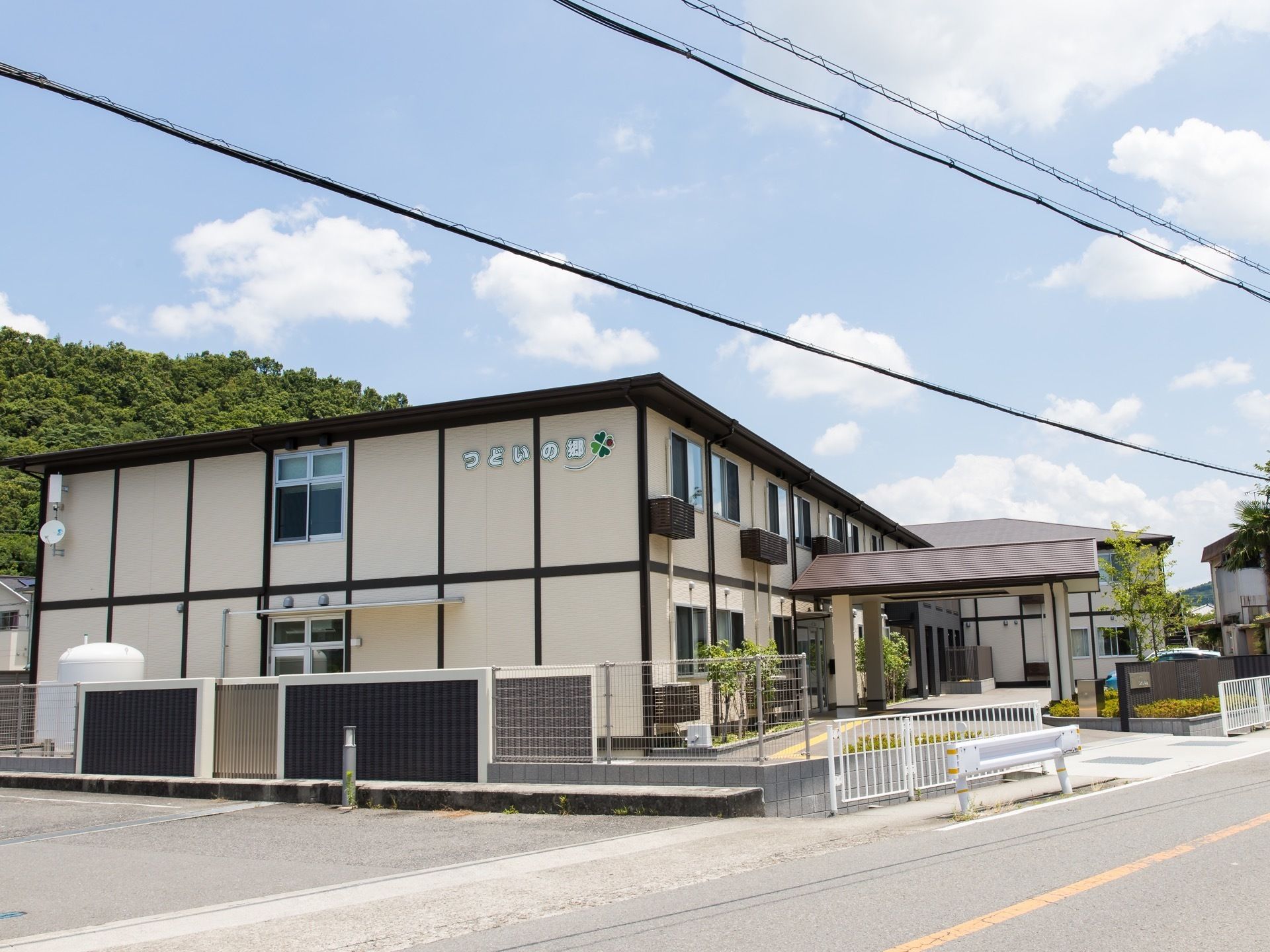 ２階建てのサービス付き高齢者向け住宅である。ベージュにダーク色のラインが、アクセントになっている。目の前は道路である。