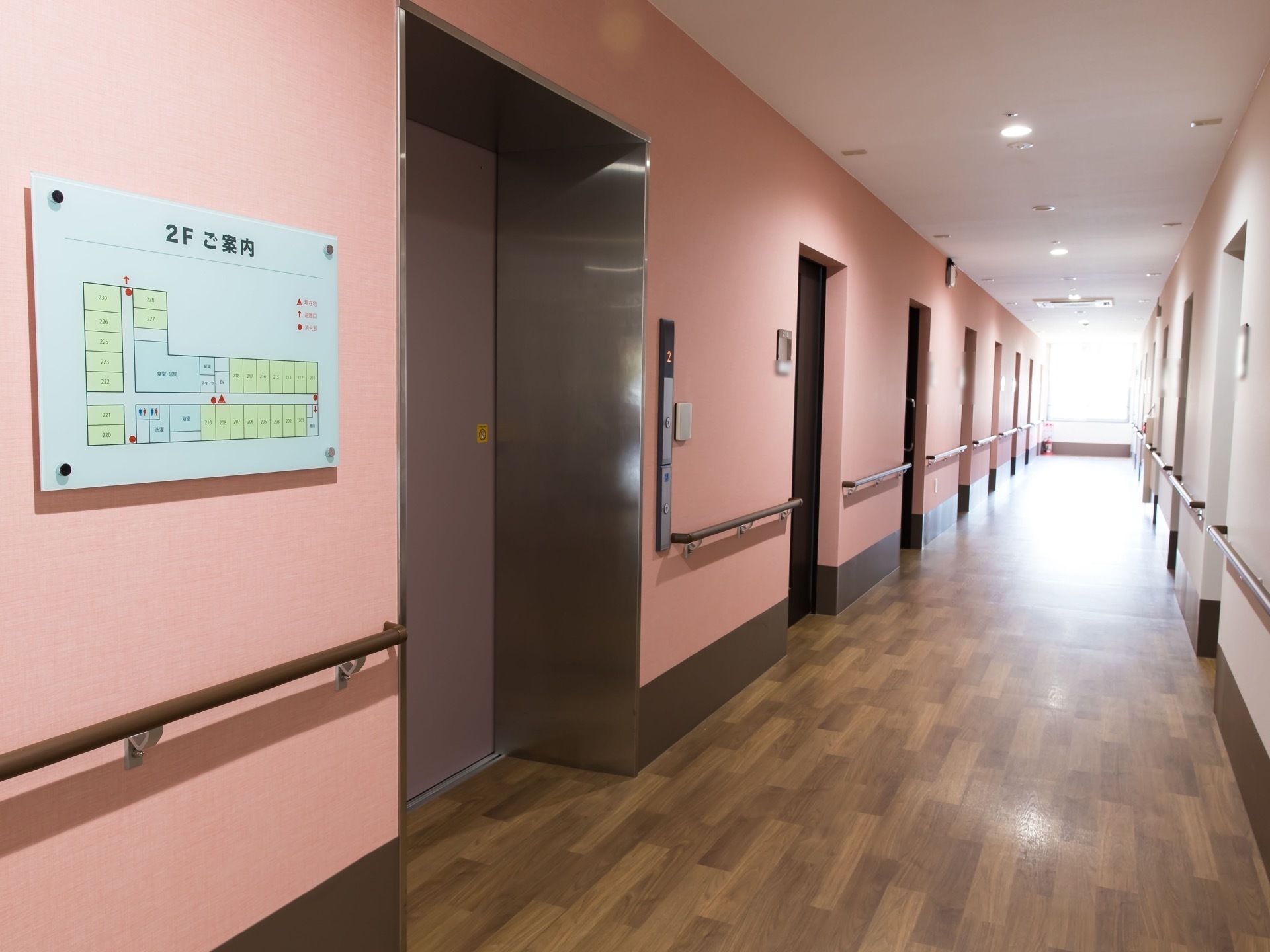 落ち着いた木目調の床色に、施された通路である。壁はあたたかいピンク色。両側には手すりが備え付けられている。