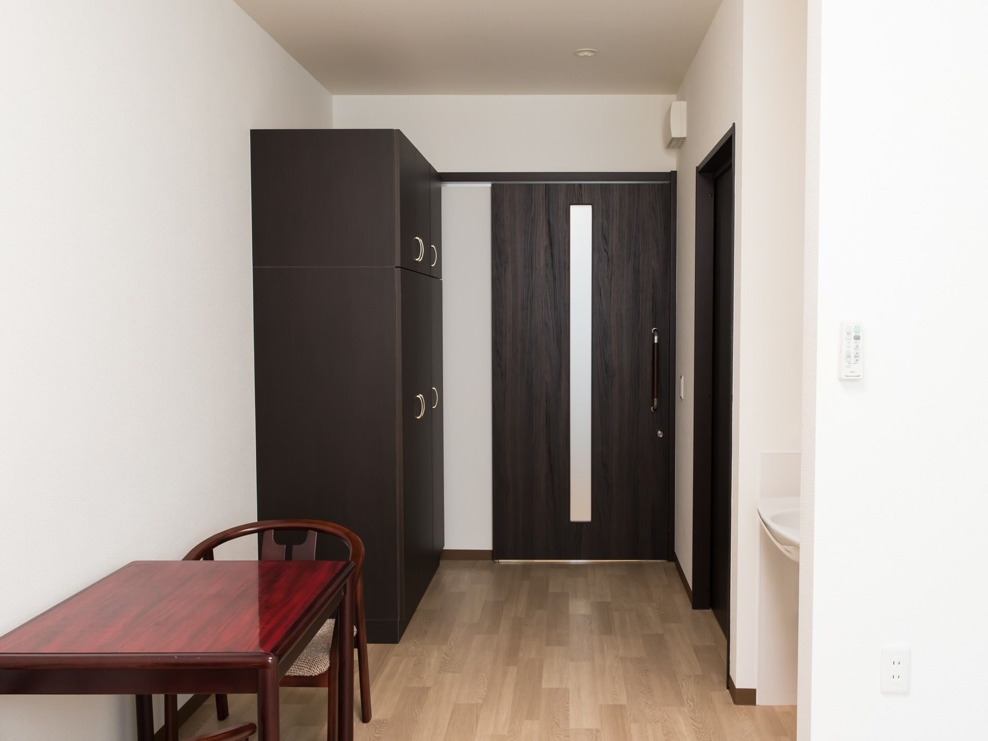 明るい色合いの床色に、ブラック系の建具が印象的な居室である。洗面台も完備。テーブルと椅子も置かれている。