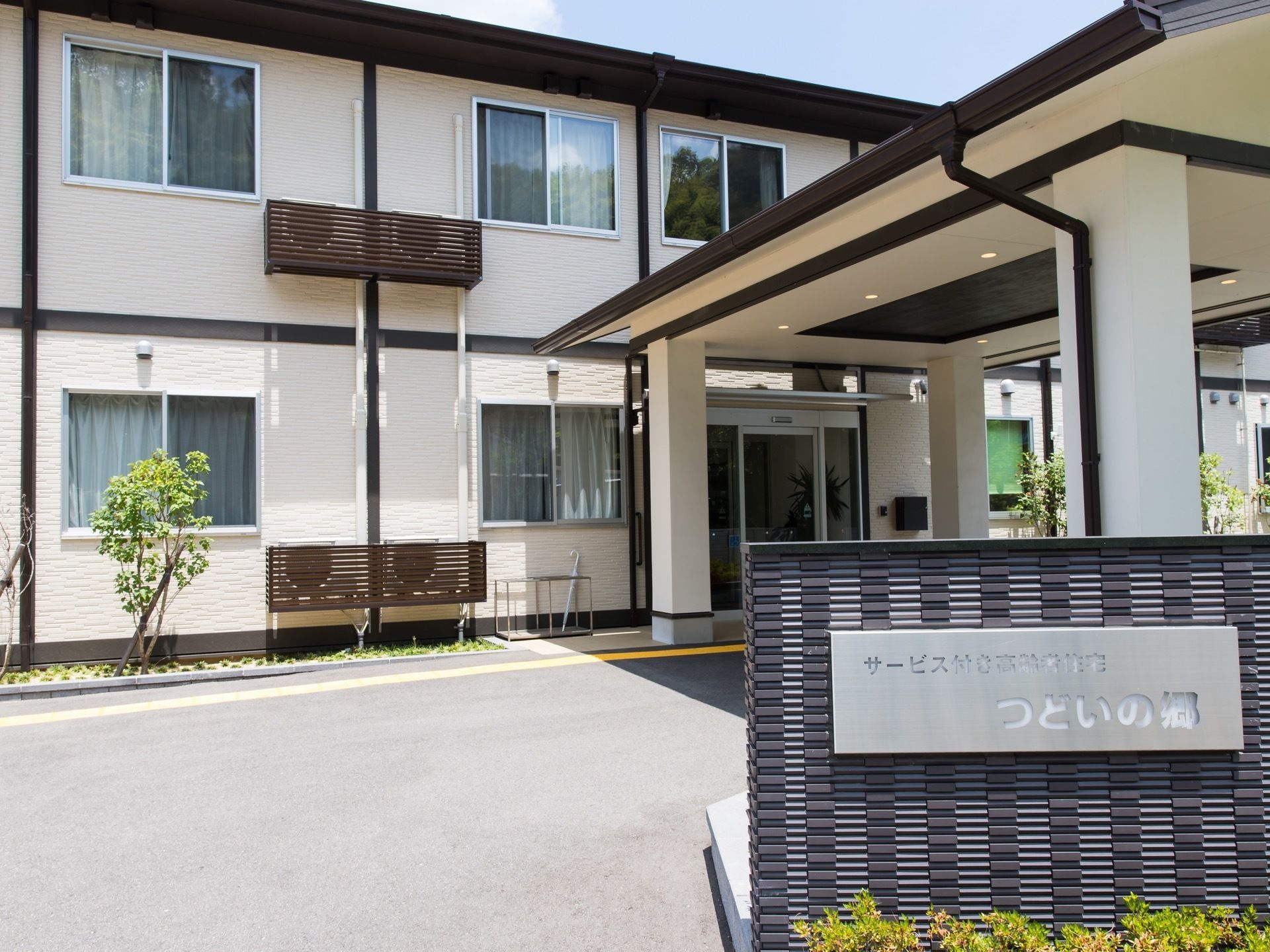 施設名が書かれた、看板が設置されている。地面はアスファルト。エントランスには、広々とした屋根が備え付けられている。