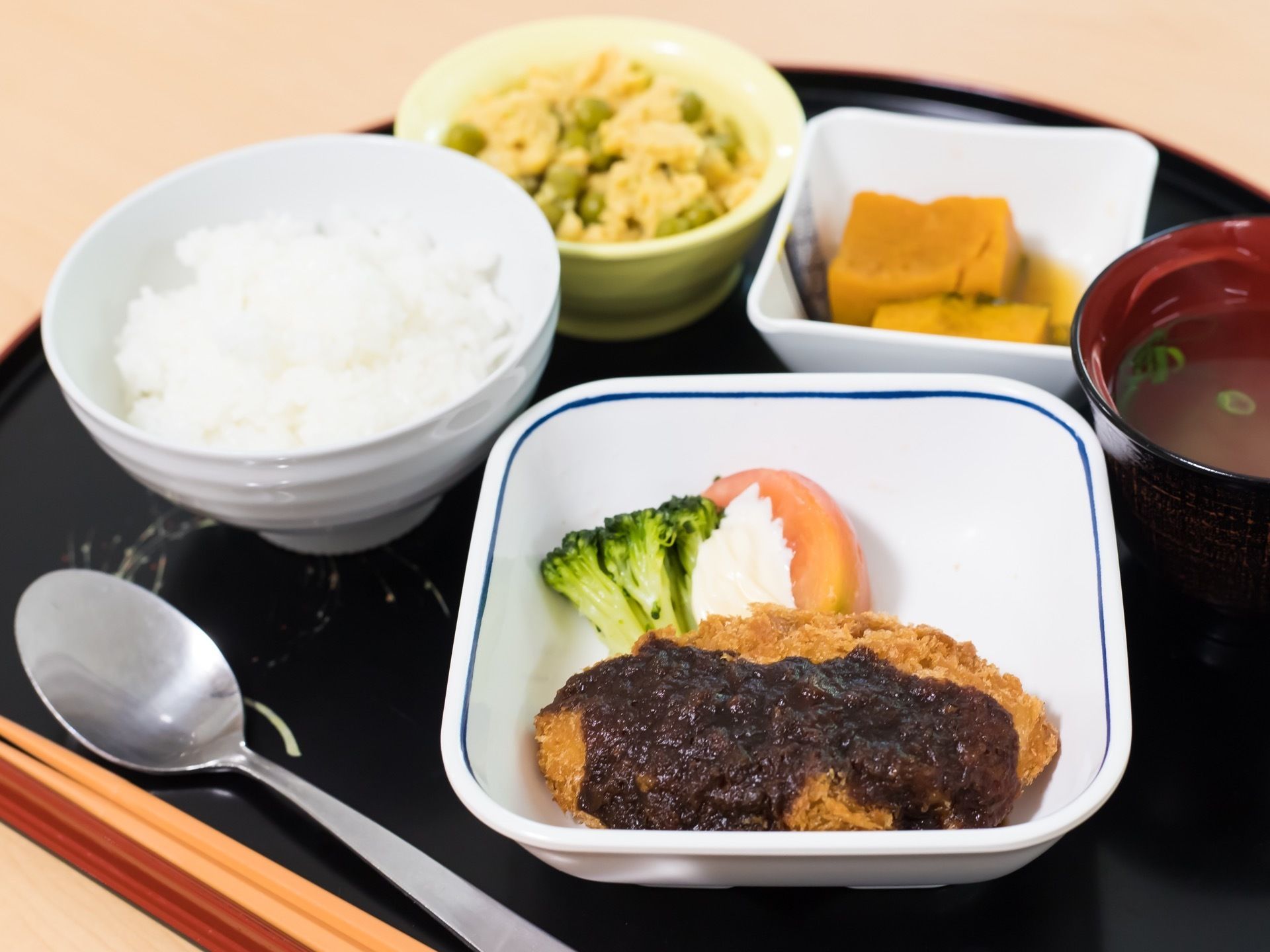 黒色の和風盆に、料理がバランスよく配置されている。本日のメニューはお肉がメイン。白ご飯やお汁、小鉢もある。