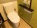グリーンの壁色が印象的な、洋式のトイレが設置されている。緊急呼び出しボタンやリモコン、手すりが備え付けられている。