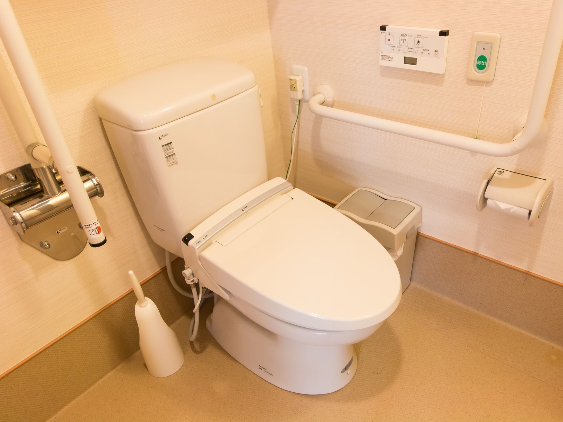 清潔感のある明るいトイレである。手すりや温水洗浄便座、ナースコール、掃除用のブラシが完備されている。