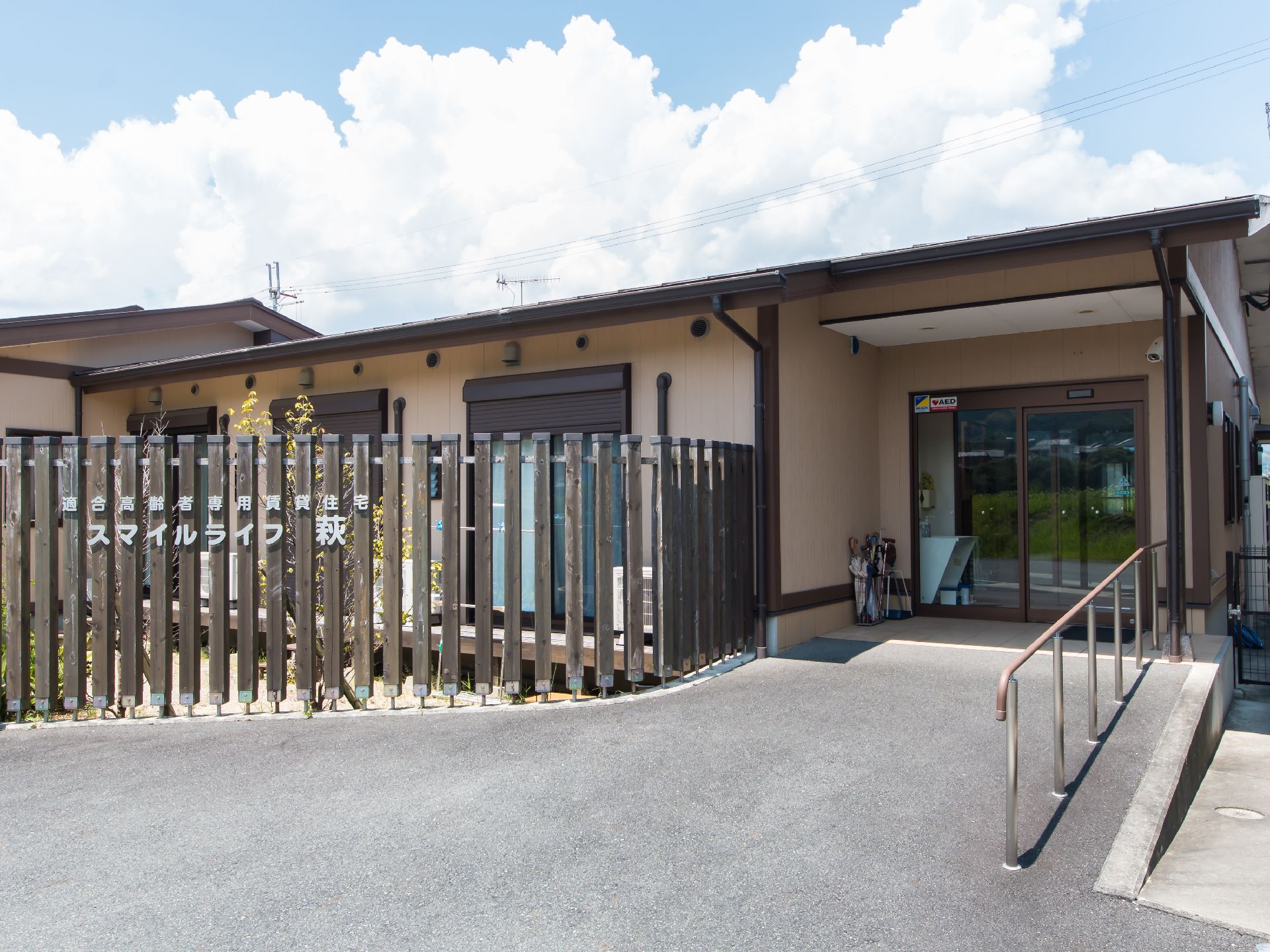 施設名称が施された木製の柵に囲まれた平屋と舗装されたスロープ