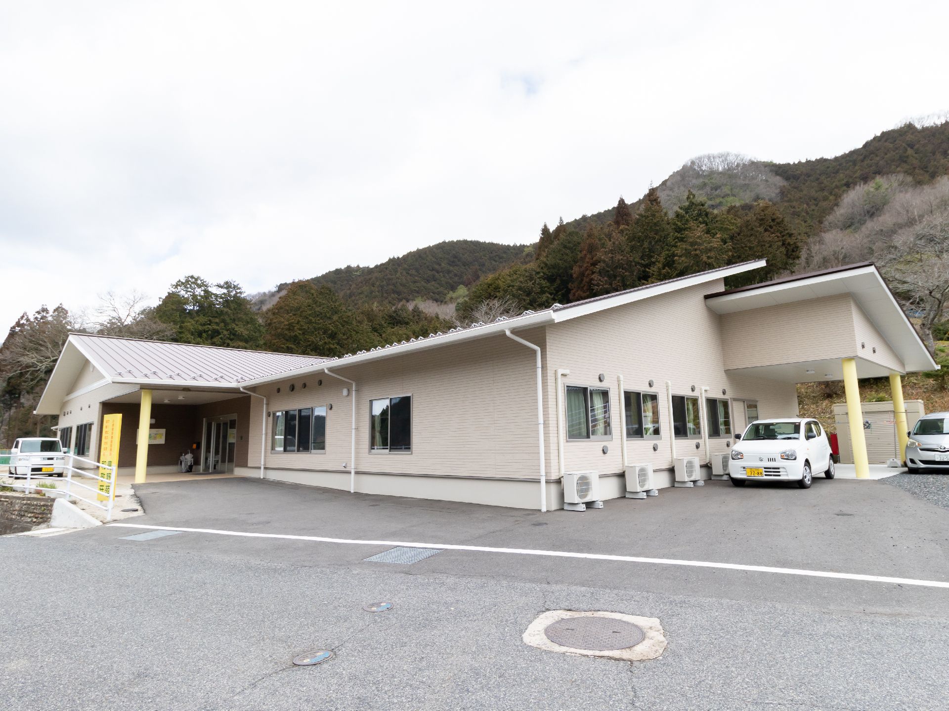 小山に囲まれた敷地に建つ白い外壁の平屋と3台の自動車