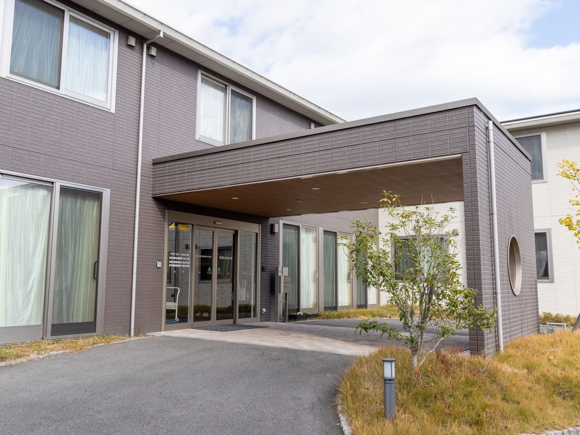 施設は２階建ての建物になっており、外壁はブラウン色である。玄関前には大きな屋根が設置されており、木々が植えられている。