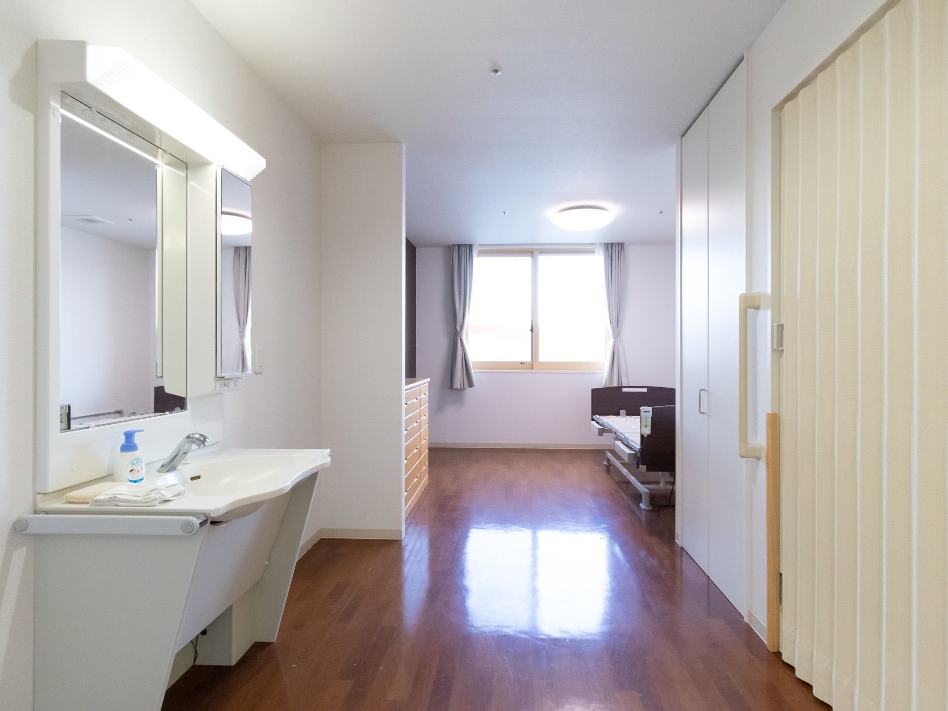 右側にクローゼットと個室トイレが設置されており、左側に洗面台がある。突き当たりの窓にカーテンが掛けられている。