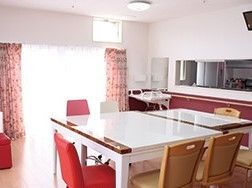 赤と白でコーディネートされたキッチンとダイニング。大きな窓が付き、白い長方形のテーブルが置かれている。