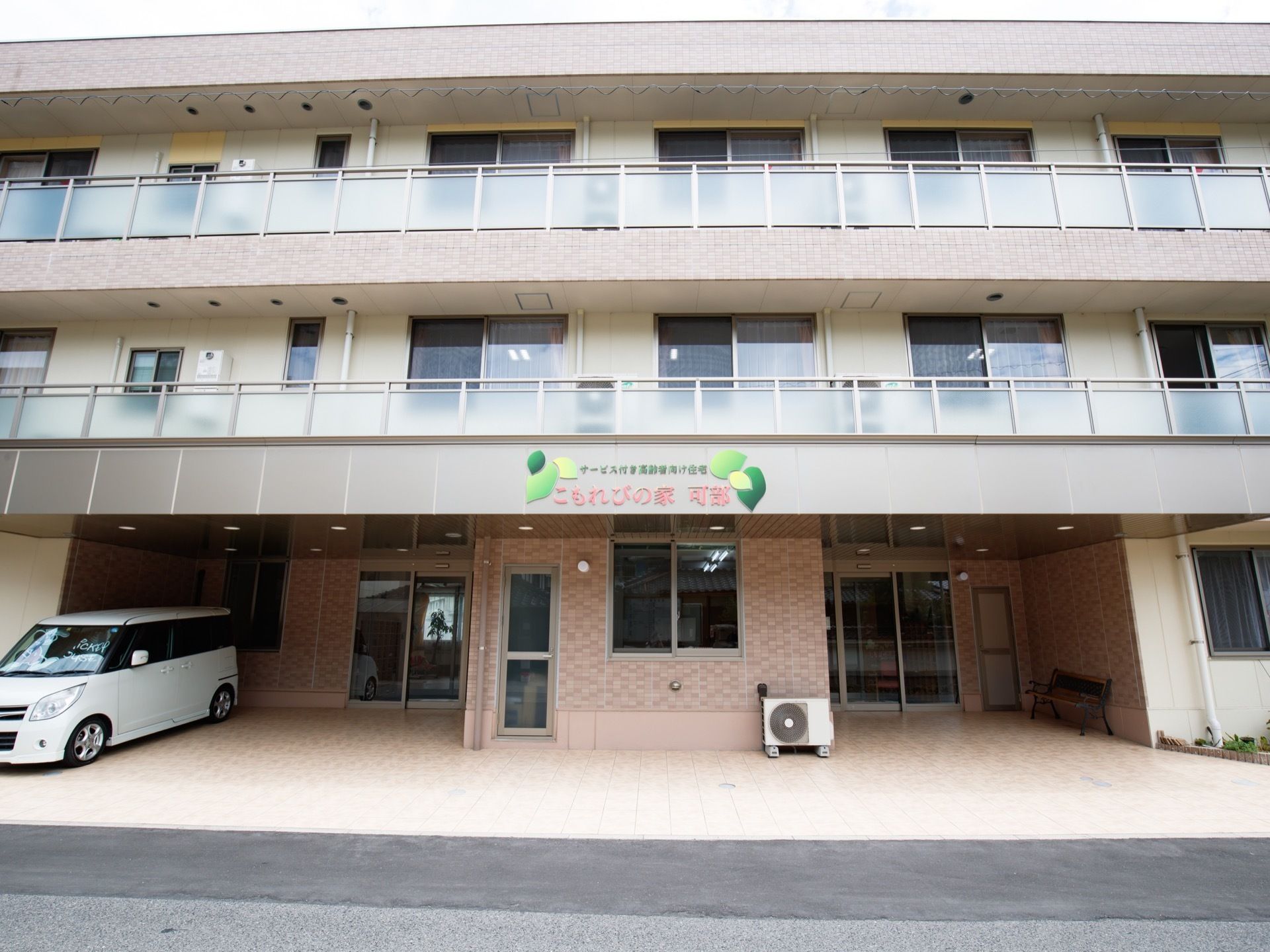 道路に面して建てられた地上３階建ての建築物である。建物の目の前に自動車が１台駐車されているのが見える。
