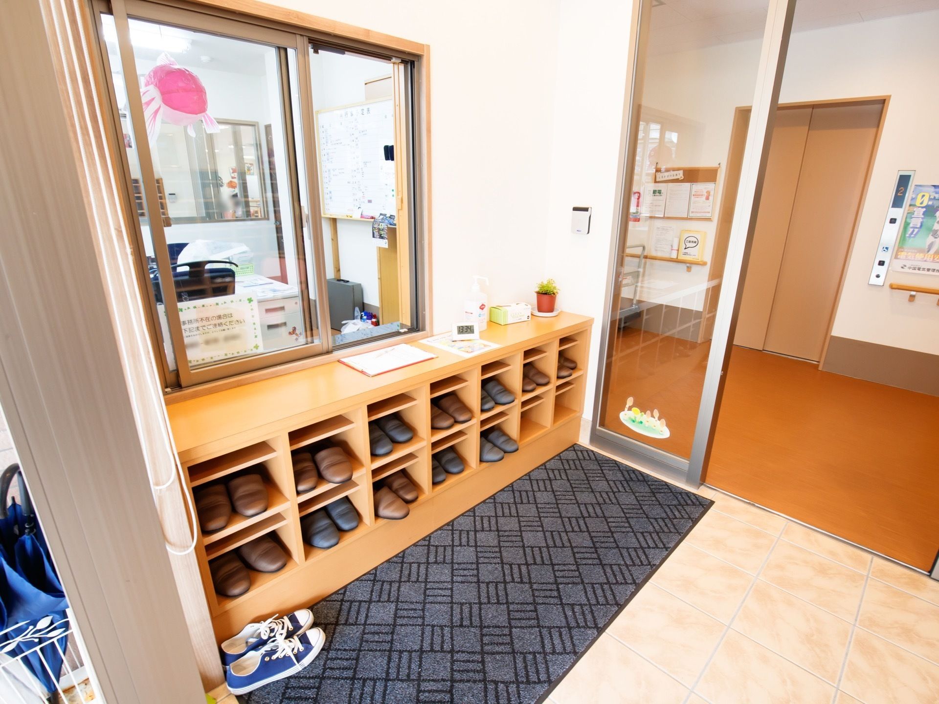 二段組みの下駄箱の中にスリッパが納められており、手前の床にはマットが敷いてある。下駄箱の上方には窓口が設置されていて、室内の様子が見える。
