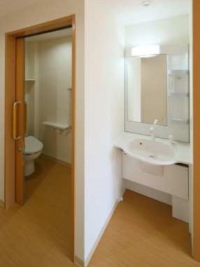 居室内にあるトイレと洗面台の写真。フットレスの洗面台、引き戸の手すり付きトイレ