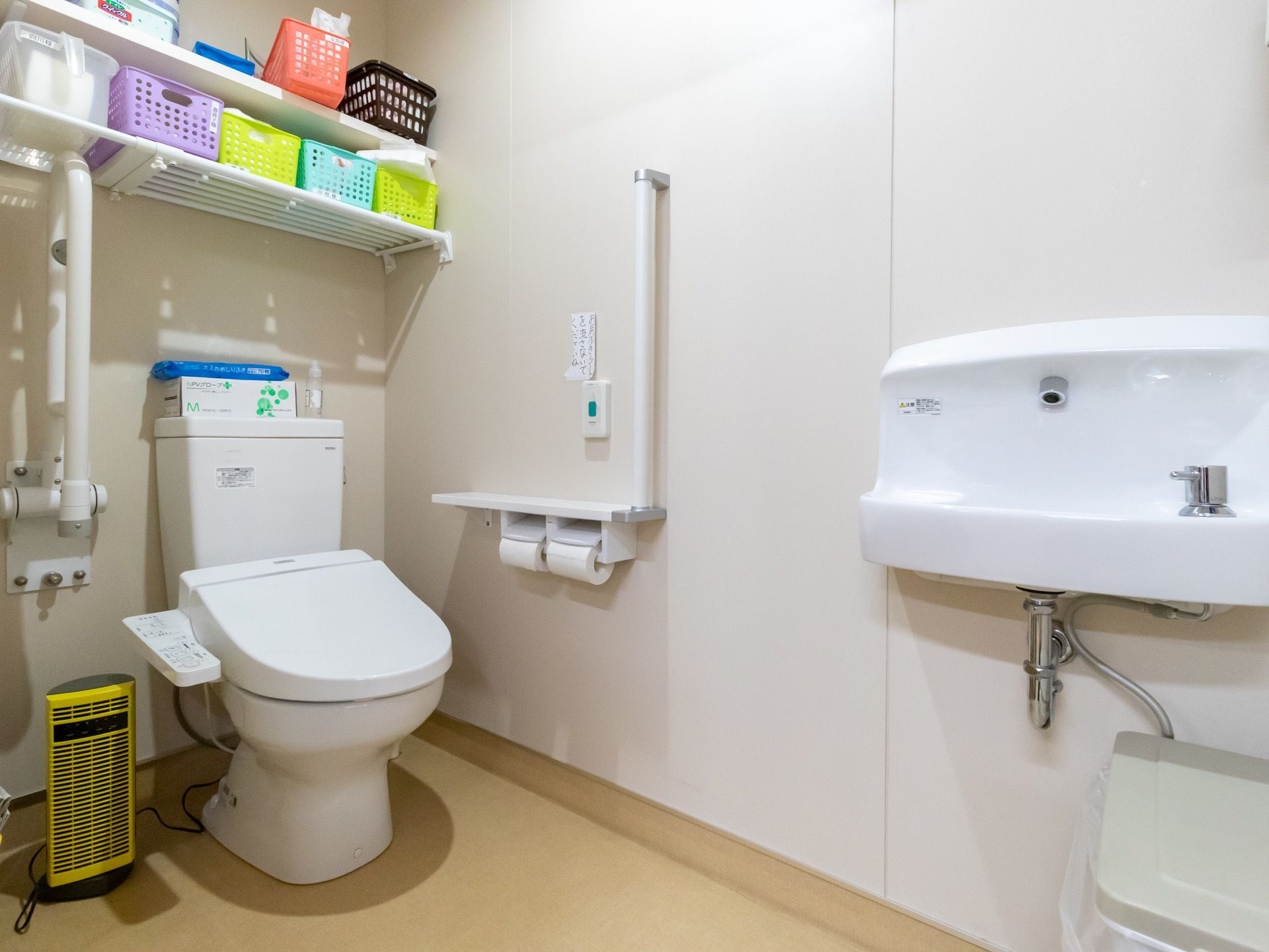 便座の両側に手すりが設置された洋式トイレがある。壁際には洗面台も付いていて、広々とした空間になっている。