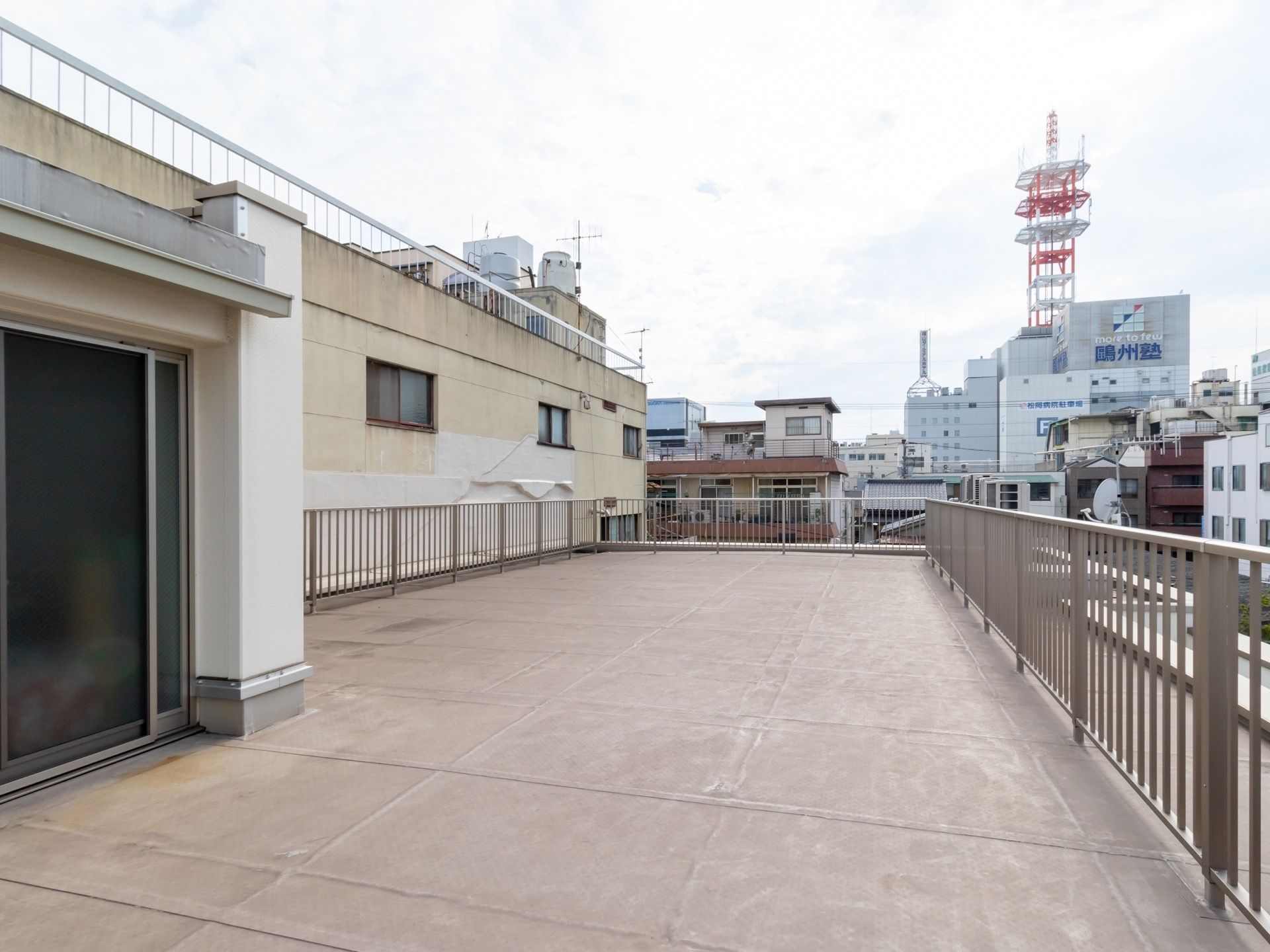掃き出し窓から外に出ると柵で囲まれた屋上があり、周辺の街並みを一望できる。近くには戸建て住宅の他、商業ビルも見える。
