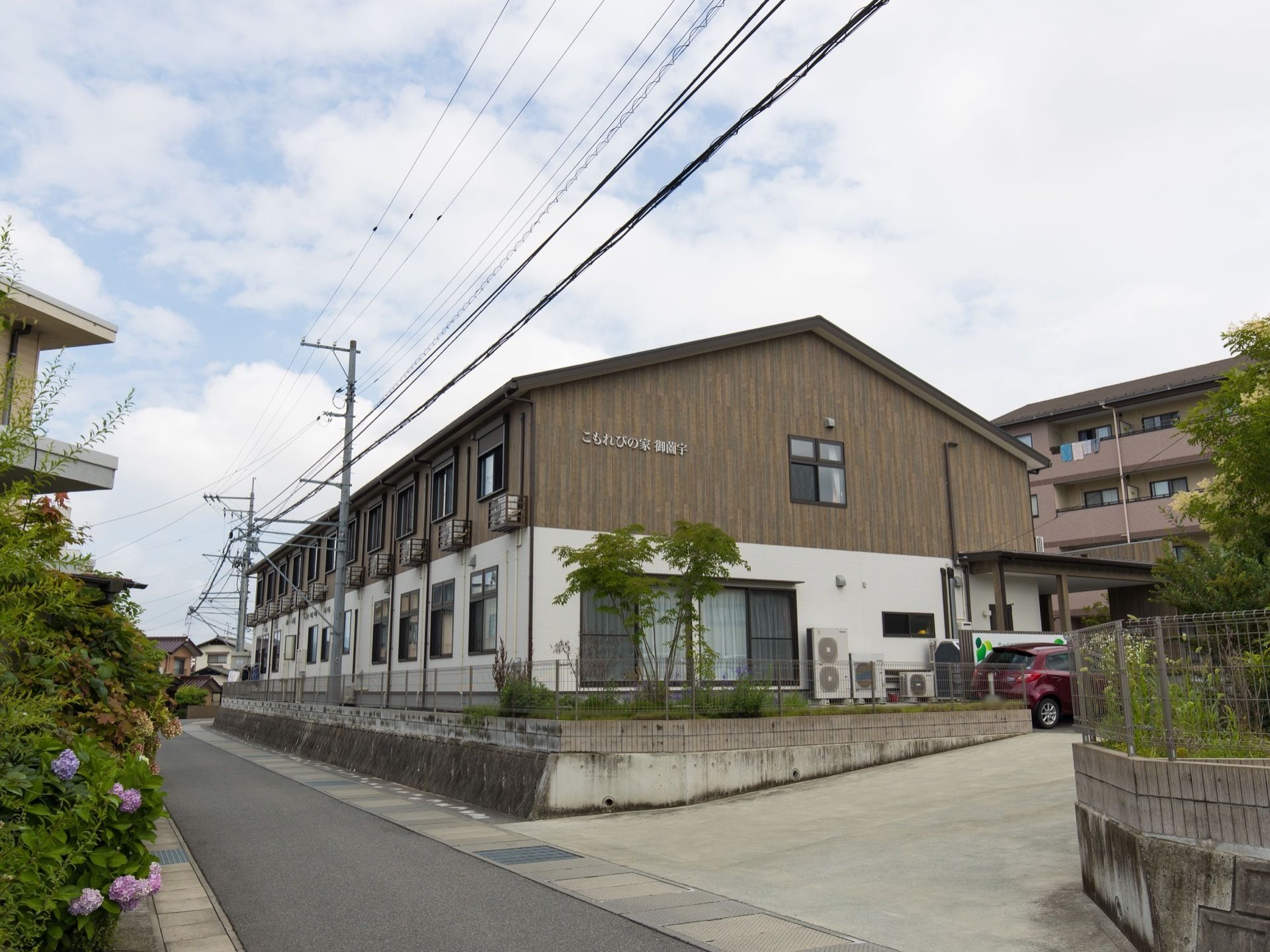 道路沿いの敷地に２階建ての施設が建っている。敷地は道路より一段高くなっており、フェンスが設置してある。