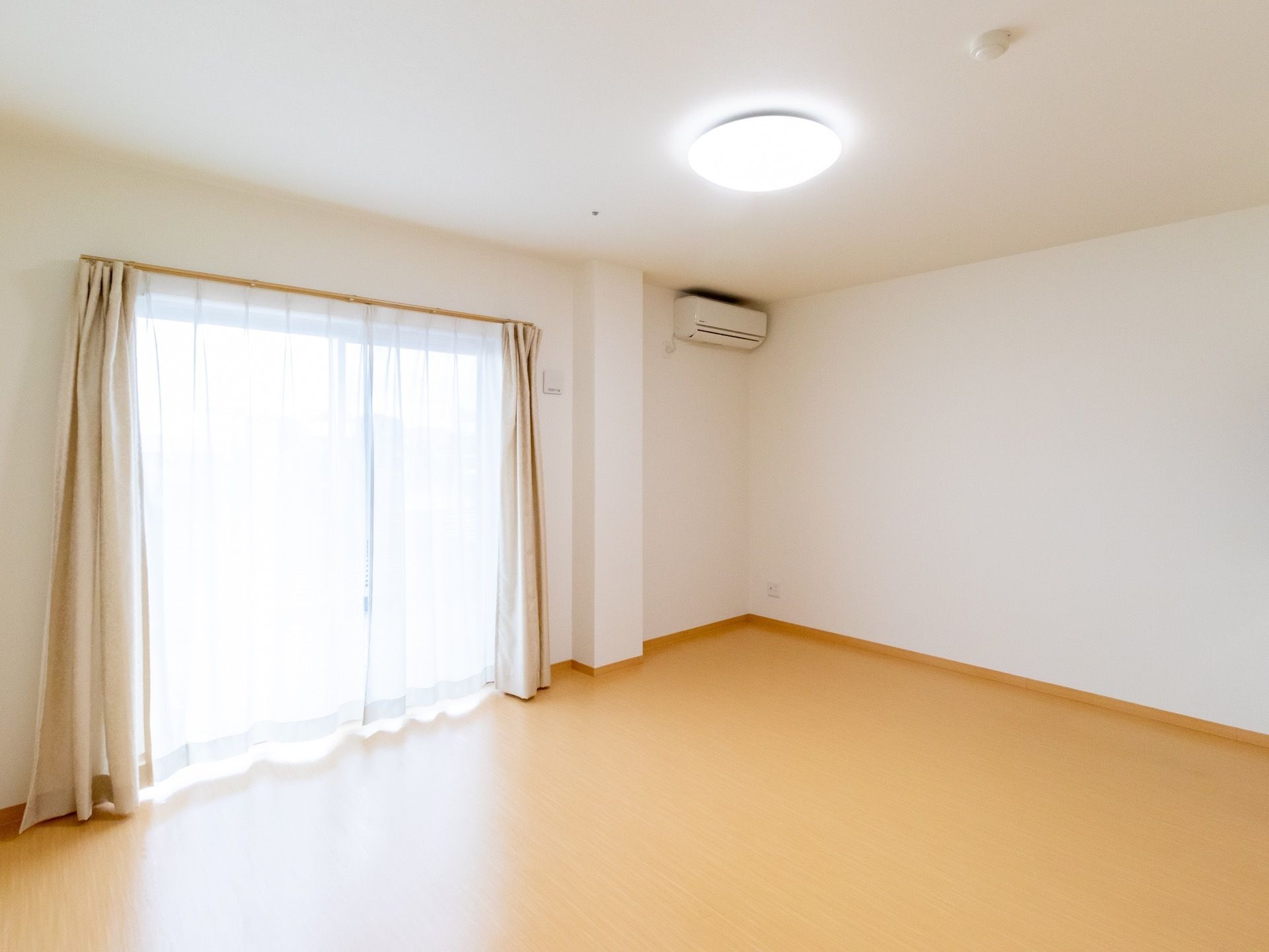 掃き出し窓からたっぷりと日の光が差し込む明るい居室である。エアコンとカーテン、LEDライトが完備されている。