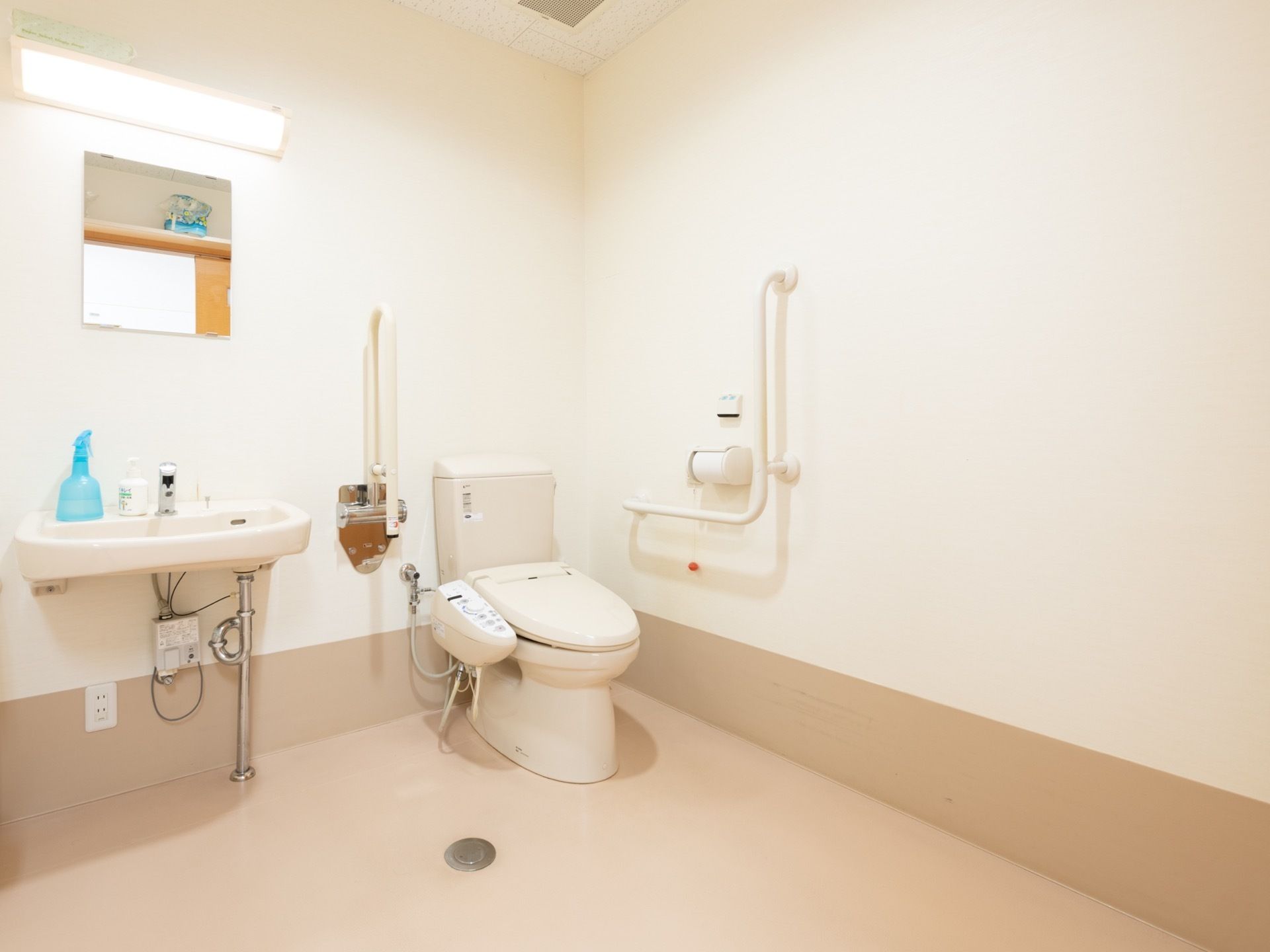 温水洗浄便座が設置されたトイレは、便座横に操作パネルが取りつけられている。壁に折り畳み式の手すりが用意されている。