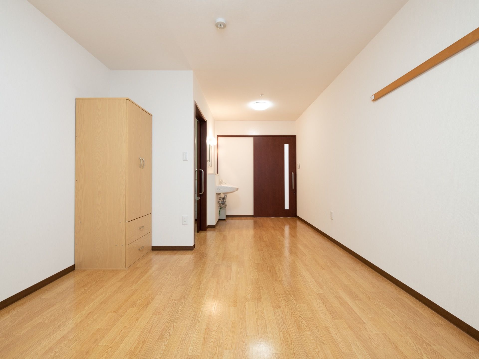 居室ドアは引き戸になっており、入ると右手に洗面台とトイレがある。居住スペースには洋服ダンスが置かれている。