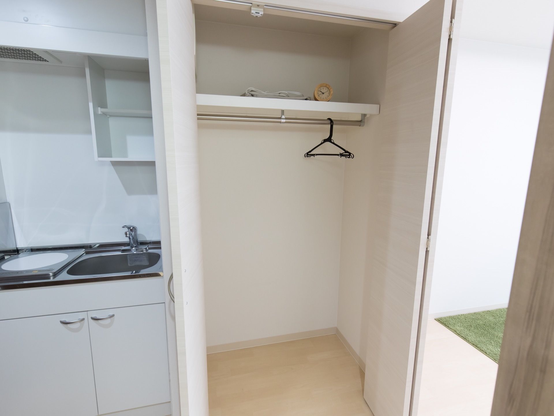左側に白いミニキッチンがある。電磁調理器がセットされている。右側にクローゼットがあり、パイプハンガーが付いている。
