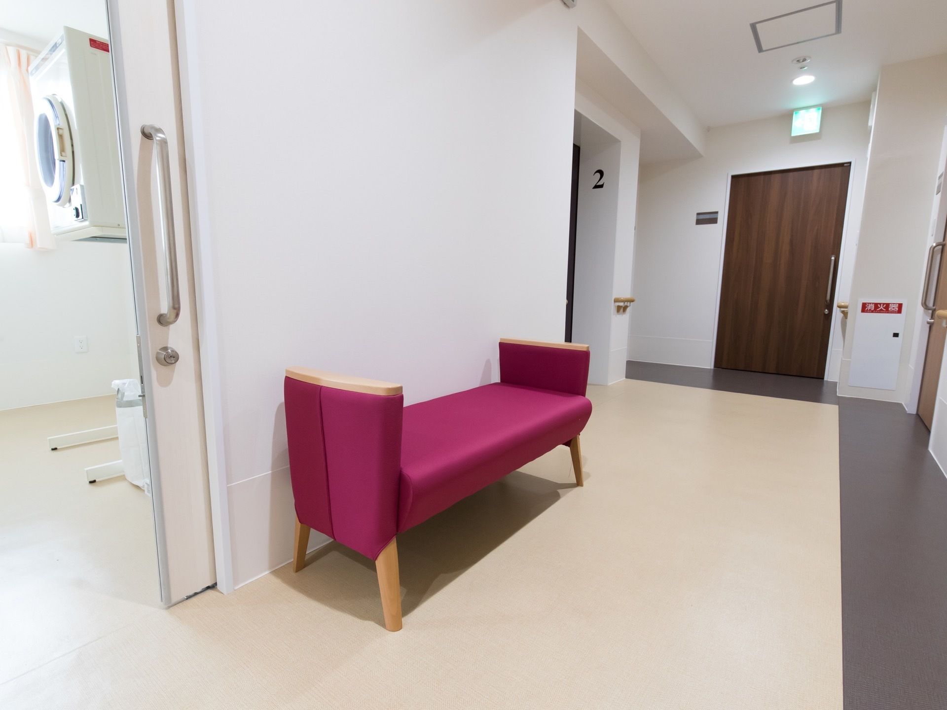 左手に引き戸式の入り口ドアを持つ部屋がある。廊下の横に折りたたみ式ベンチが置かれている。正面の部屋の横に、消火器ボックスがある。