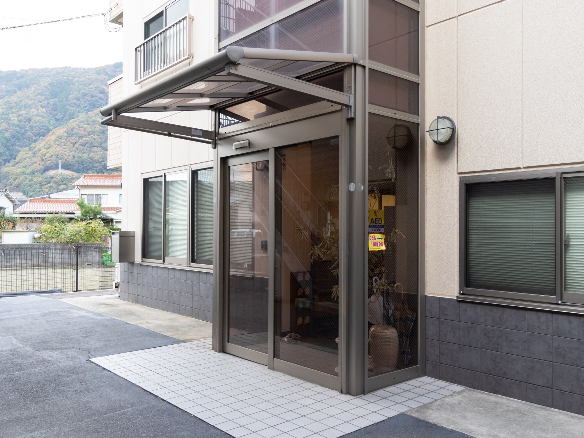 玄関は半透明のガラスの自動扉である。玄関前にちょっとしたひさしがあり、その下はタイル敷きになっている。