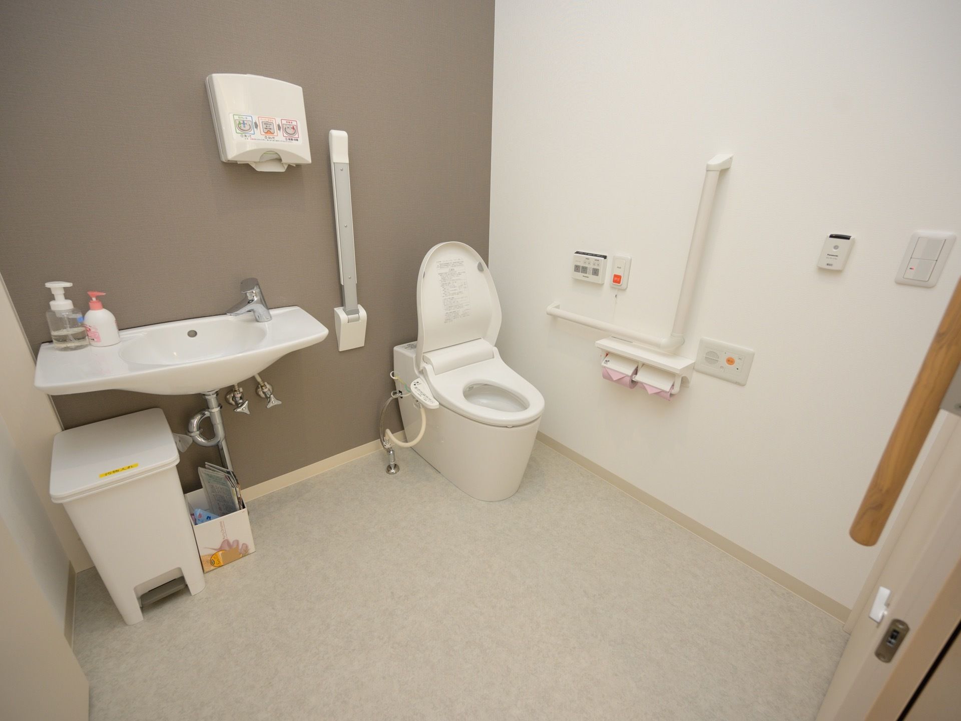 広々としたトイレは白とグレーを基調としており清潔感がある。手すりが完備されており、片側は折りたたみ式である。