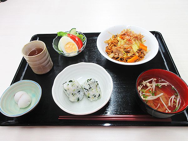 おにぎりや焼きそば、みそ汁、サラダなどが並んだ黒いトレーには箸も置かれている。
