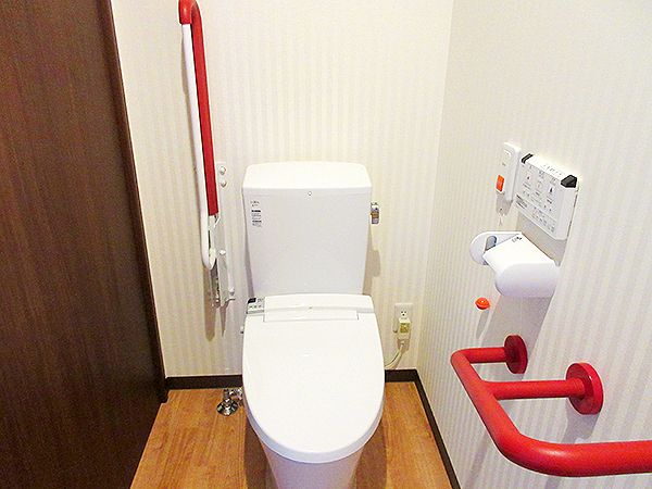 オレンジの呼び出しボタンや赤い手すりが付いたトイレは白を基調としていて、フロアはフローリング。