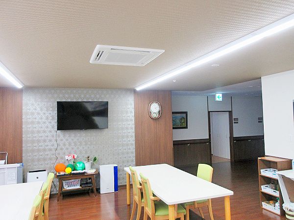 大きな壁掛けテレビが付いたリビングダイニング。グリーンの椅子がセットされたダイニングテーブルセットが置かれている。