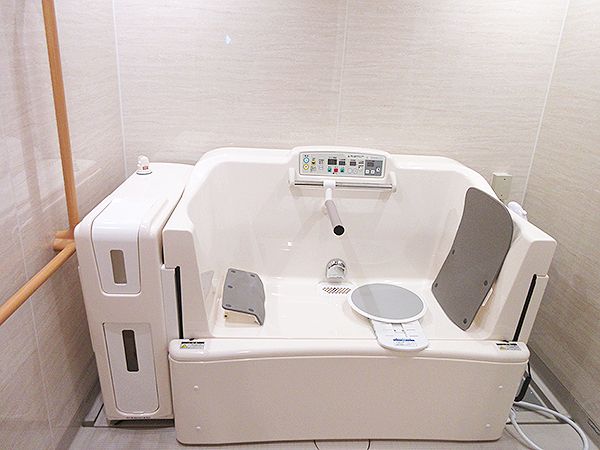 浴槽の壁が一部スライドする機会が設置された浴室。機械にはフットレストや背もたれもあり、ホースのようなものもある。