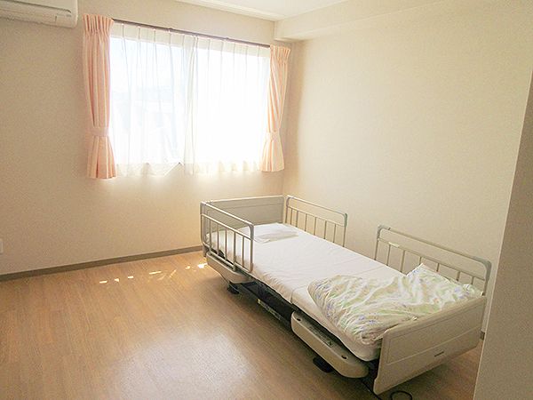 エアコンが付いたフローリングの部屋には寝具付きのベッドやカーテンが付いた窓がある。