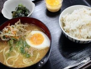 卵や野菜が乗ったラーメンや白いご飯、デザート、青菜の和え物などが並んでいる黒いトレー。