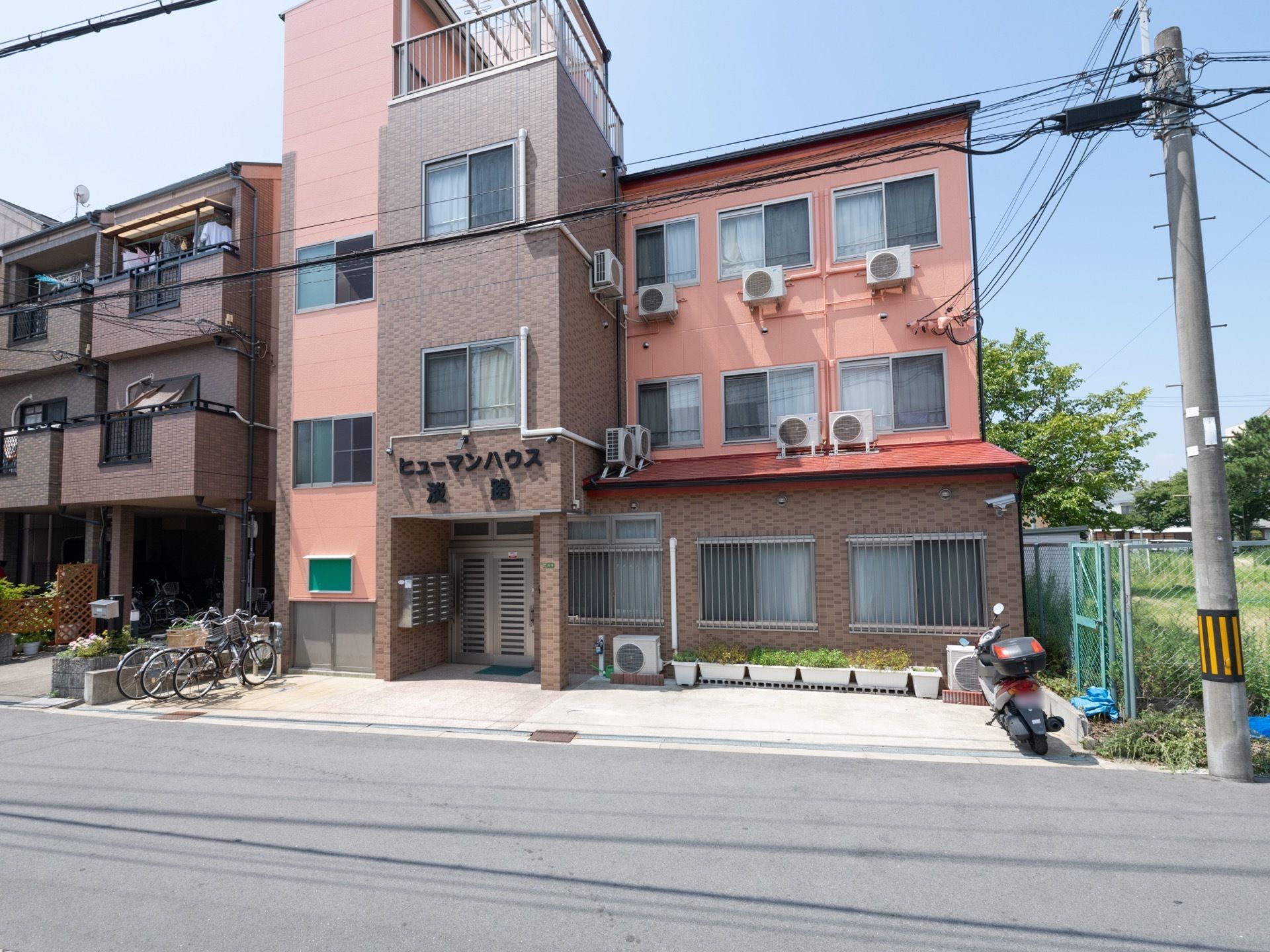 道路と敷地との段差がないので、車椅子でも道路に出やすい。施設の前に、自転車が３台、オートバイが１台駐まっている。