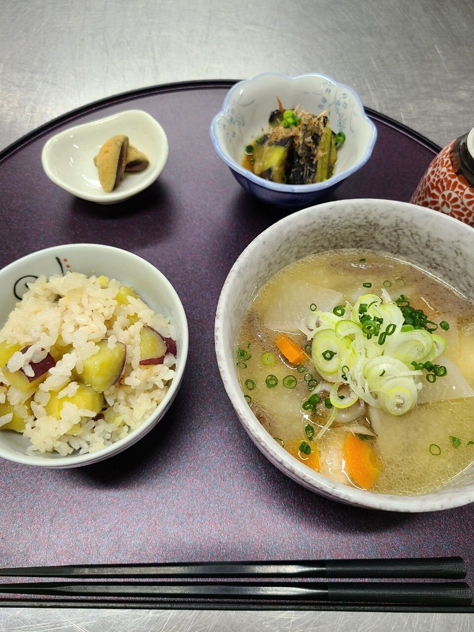 天ぷらの盛り合わせや白いご飯に吸い物、野菜の小鉢などがならんだ赤いトレー。カットフルーツも添えられている。