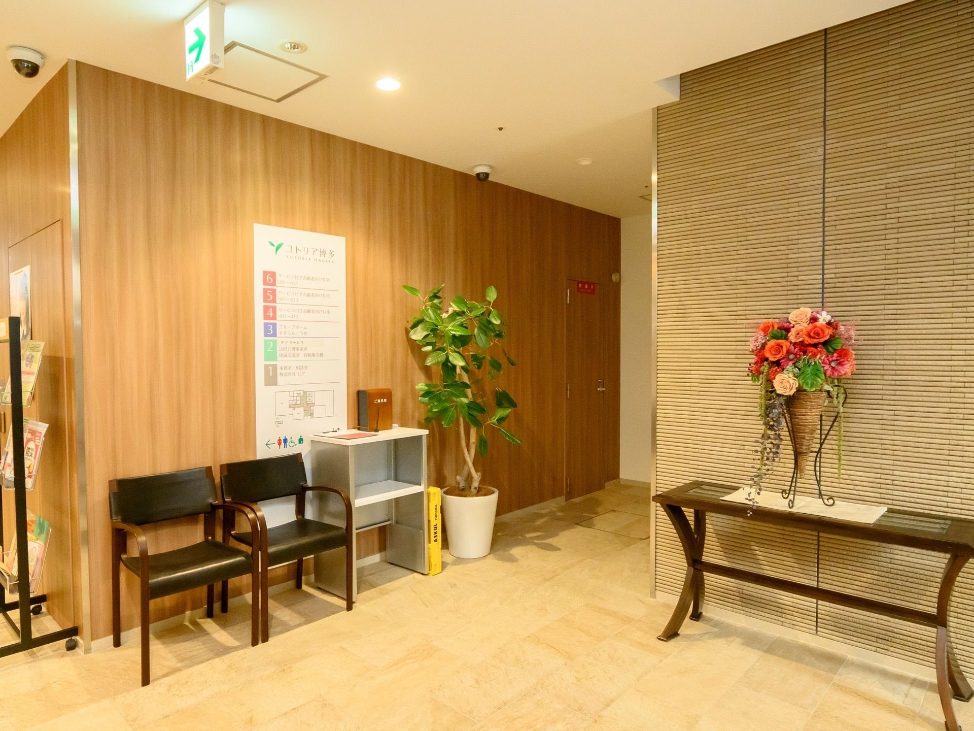 ゆとりのある廊下になっている。大きな花や、観葉植物が置かれている。施設の館内図が壁に掲示されている。