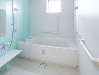 さわやかなグリーンと白の浴室。一人用の浴槽が設置され、シャワーや手すりもついている。