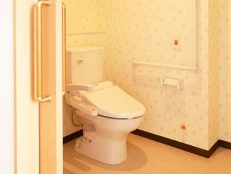引き戸を開けると広いトイレがあり、壁には呼び出しボタンやエル字型の手すりが付いている。