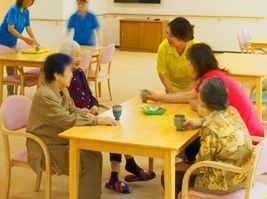 食堂のテーブルについて話している入居者3名とスタッフ2名。テーブルの上にはお茶とお菓子が置かれている。