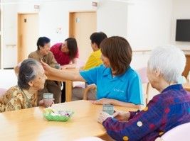 水色のポロシャツを着た女性スタッフが、二人の女性入居者と一緒に話をしている様子。