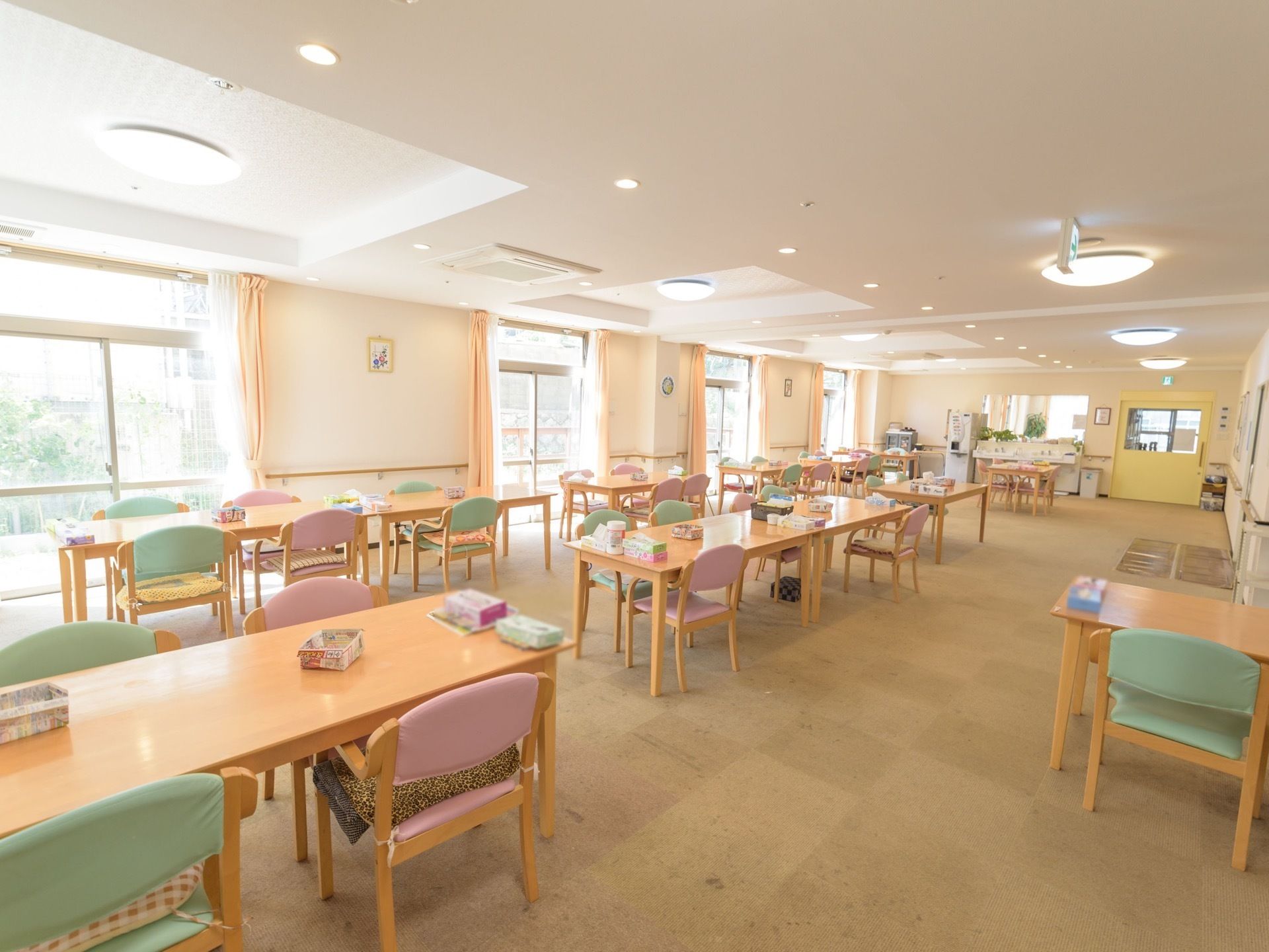 大きなテーブルとグリーンとピンクの椅子が交互に並んでいる広い食堂がある。壁面は大きな窓になっており、外光が差し込んでいて明るい。