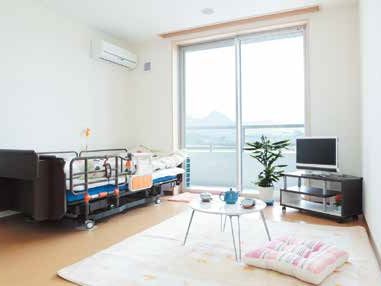 大きな窓が付いたフローリングの部屋には寝具付きのベッドやカーペット、ローテーブルがあり、観葉植物が飾られている。